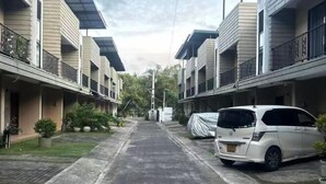 Une rue résidentielle bordée de maisons à deux étages, avec un fourgon blanc garé et une allée couverte.
