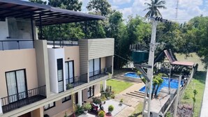 Un immeuble moderne à plusieurs étages, doté de balcons, d’une piscine et d’un jardin bien entretenu.