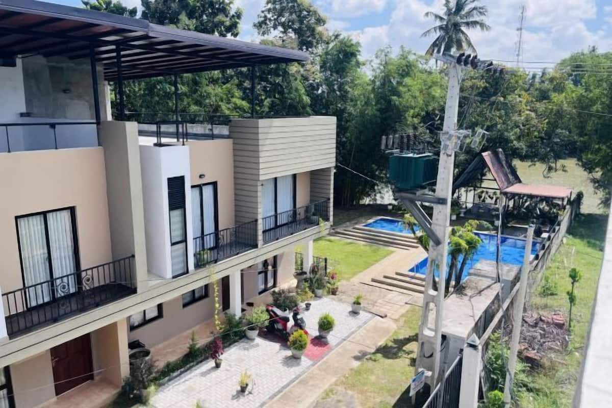 A modern multi-story building with balconies, a swimming pool, and a well-maintained garden.