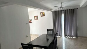 Un coin repas avec une table et des chaises, un ventilateur de plafond et une vue sur l’extérieur, visible à travers une porte.
