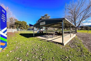 A covered outdoor seating area with tables and benches, surrounded by grass and trees. - Nature Lovers: Snowy Cottage Escape! Book Direct (Talbingo)