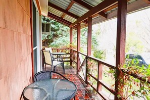 A covered balcony with a table and chairs, a view of a car, and a wooden wall. - Nature Lovers: Snowy Cottage Escape! Book Direct (Talbingo)