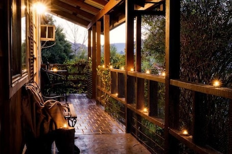 A covered outdoor seating area with a wooden bench, a table, and string lights.. Nature Lovers: Snowy Cottage Escape! Book Direct