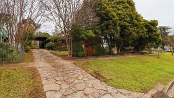A stone pathway leading to a house with a covered porch, surrounded by trees and a grassy yard.