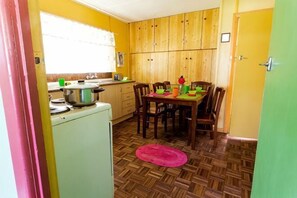 Una cocina compacta con armarios de madera, una mesa de comedor con sillas, un refrigerador y una ventana con persianas.