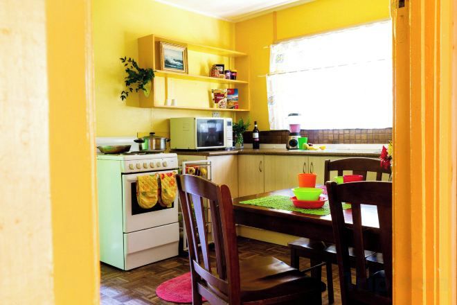 A kitchen with a stove, microwave, and cabinets. There is a dining table with chairs and a window with blinds.
