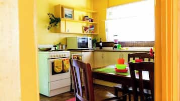 A kitchen with a stove, microwave, and cabinets. There is a dining table with chairs and a window with blinds.