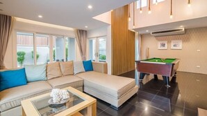A modern living room with a sofa, a glass coffee table, and a pool table. - Olivia Beach Sea and Sky Pool Villa Hua Hin (Cha-am)