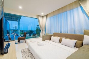 A modern hotel room with a large bed, a TV, and a balcony with a view of a cityscape. - Olivia Beach Sea and Sky Pool Villa Hua Hin (Cha-am)