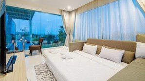 A modern hotel room with a large bed, a TV, and a balcony with a view of the city. - Olivia Beach Sea and Sky Pool Villa Hua Hin (Cha-am)