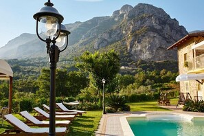 A poolside area with lounge chairs, a lamp post, and a view of mountains.