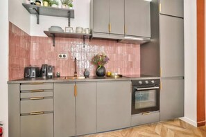 A kitchen with grey cabinets, a stainless steel oven, and a pink tiled backsplash. - NEW! Eiffel Tour Splendid 2BR apt in Paris (Paris)