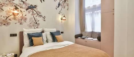 Une chambre à coucher avec un lit, des oreillers, une table de chevet, une fenêtre avec des rideaux et des lampes fixées au mur.