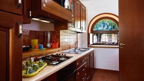 Une cuisine de taille réduite, dotée de meubles en bois, d’une cuisinière à gaz et d’une fenêtre à arc.