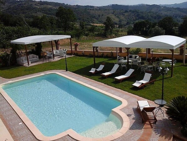 A rectangular swimming pool with a curved edge, surrounded by a patio area with lounge chairs and umbrellas.