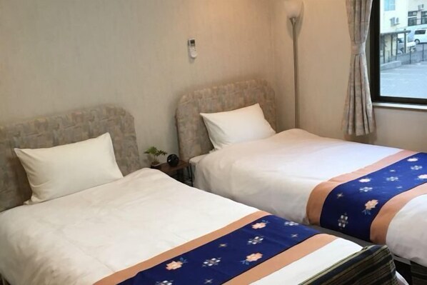 Dos camas individuales con sábanas blancas y colchas de flores azules en una habitación de hotel.