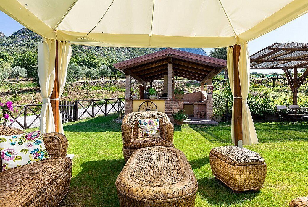 A covered outdoor seating area with wicker furniture and a brick structure in the background.