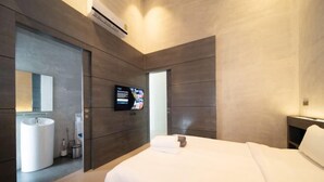 A modern hotel room with a large bed, a television, a bathroom with a sink and mirror, and wooden paneling.