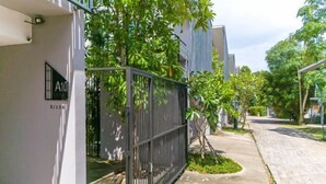 A residential area with a gated entrance, a paved sidewalk, and lush greenery.