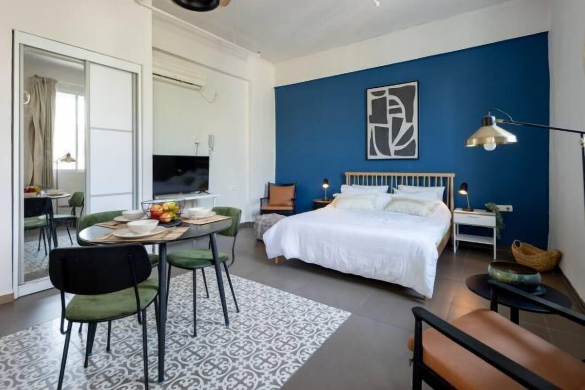 A bedroom with a bed, bedside tables, a TV, and a dining area with chairs and a table.