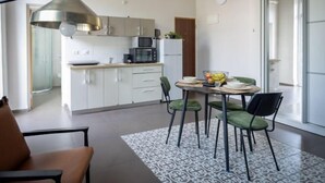 A modern kitchen with white cabinets, a microwave, and a dining area with a table and chairs. - The Printhouse Boutique Studio 4 (Haifa)