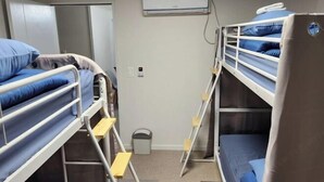 Et sovesal med køjesenge, en hvid aircondition, en dør og en skraldespand.