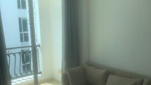 Una habitación con un sofá color beige, una ventana con vista a un edificio y un balcón con barandilla.