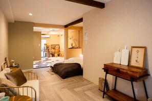 A hotel room with a bed, a sofa, a wooden side table, and a hallway leading to another room. - Dream traveler (Osaka)