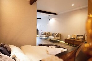A modern hotel room with a bed, a seating area with a sofa and chairs, a wooden side table, and a wall-mounted light fixture. - Dream traveler (Osaka)