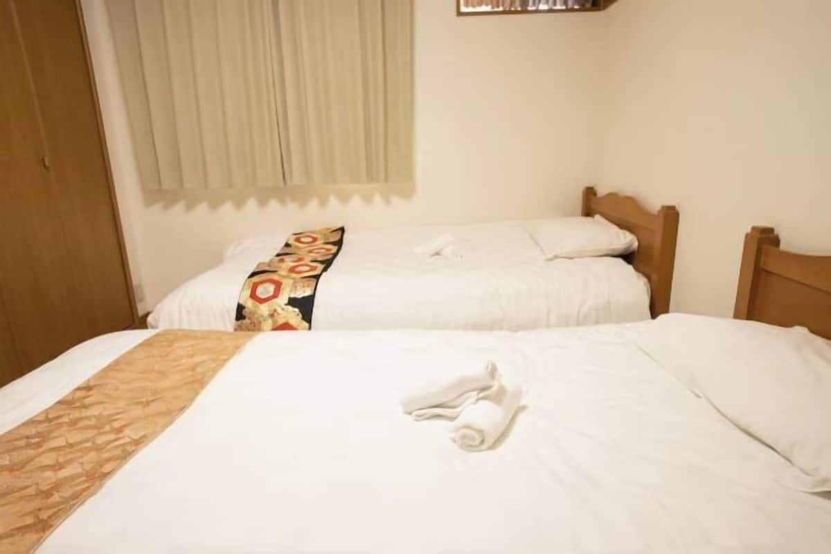 A hotel room with two single beds, a wooden headboard, a window with curtains, and a wooden wardrobe.