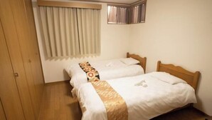 Une chambre d’hôtel avec deux lits simples, une armoire en bois, une fenêtre avec des rideaux et un petit miroir au mur.