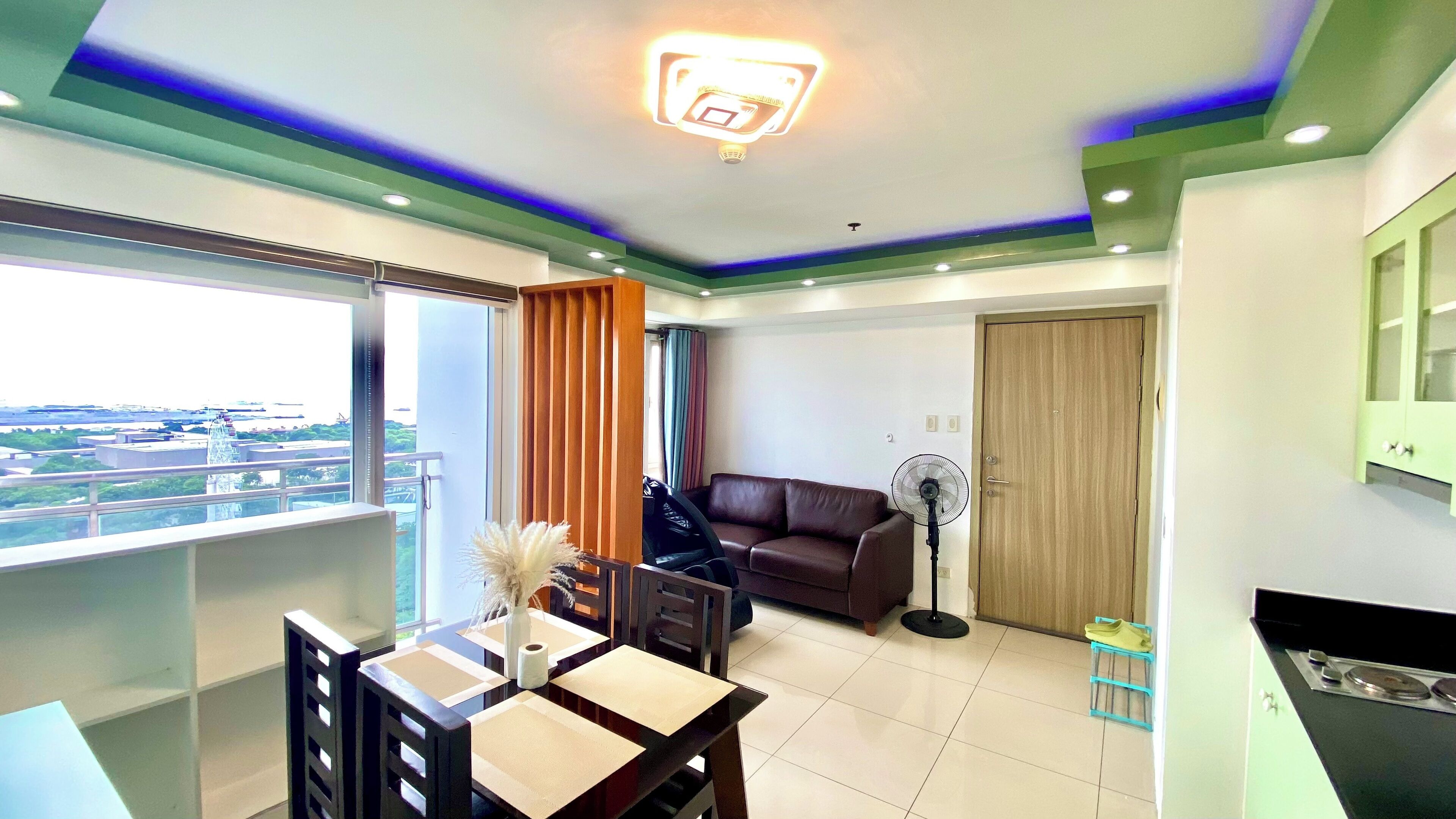 A modern living room with a view of a cityscape, a dining area with a table and chairs, and a kitchenette with a stove.