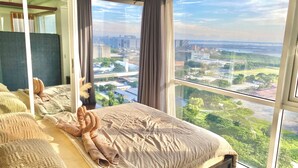 Una camera da letto con un'ampia finestra che si affaccia sulla città, un letto con asciugamani arrotolati e vista su un ponte e degli edifici.