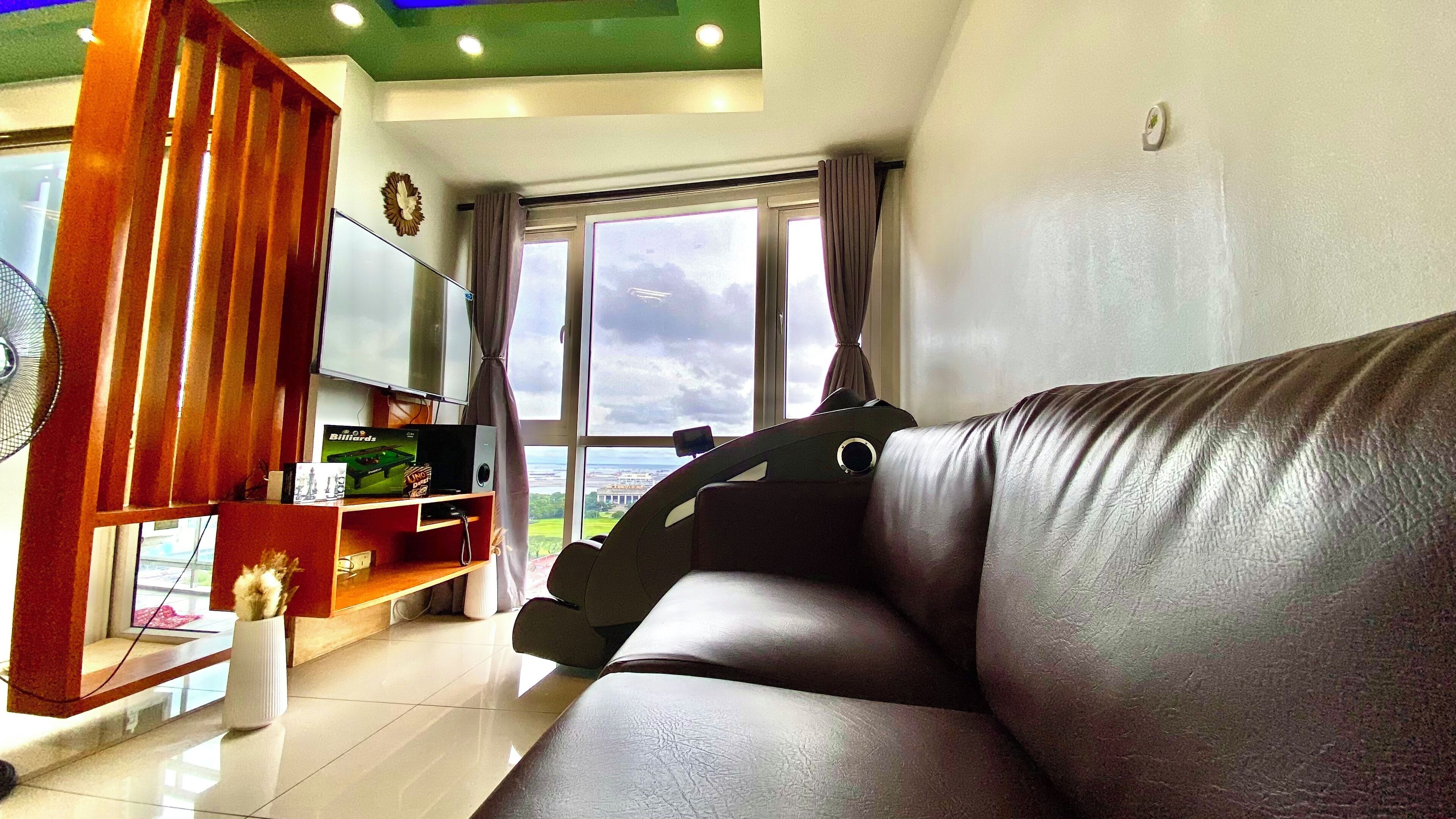 A modern living room with a leather sofa, a wooden entertainment unit, and a large window offering a view of a cityscape.