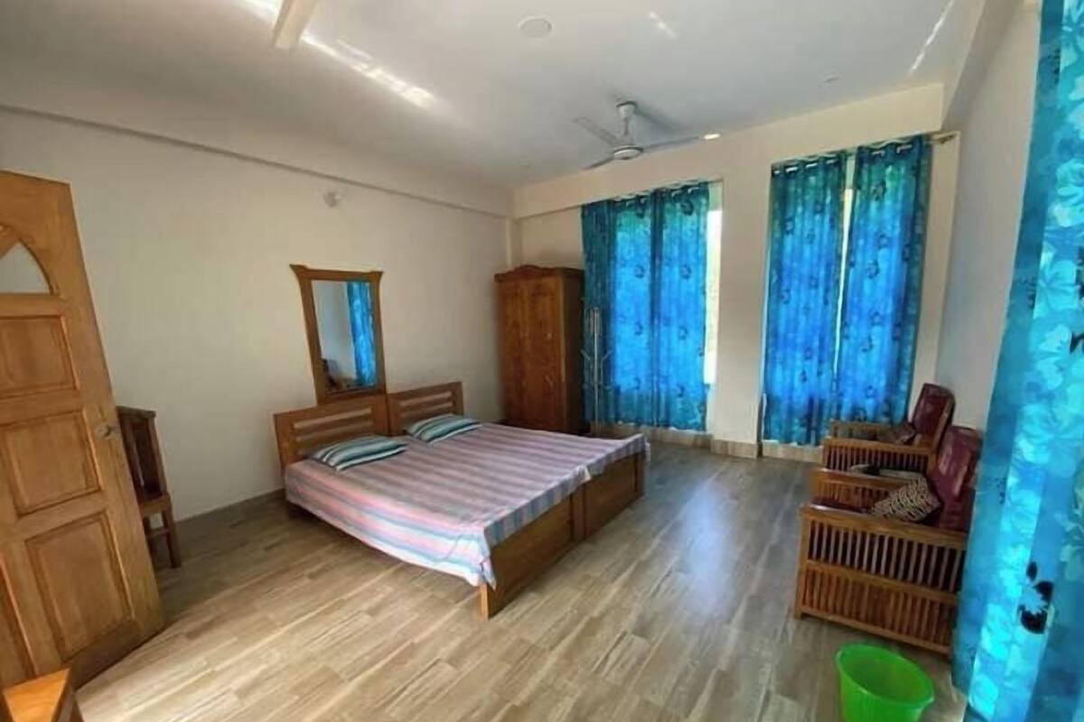 A bedroom with a large bed, wooden wardrobe, and a green bucket.
