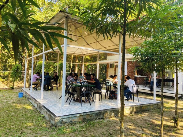 Un espace extérieur aménagé pour les repas, avec un pavillon couvert, des tables et des chaises.
