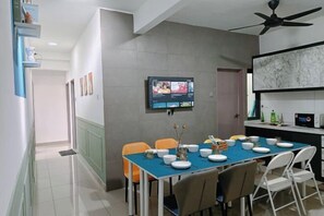 Ein moderner Essbereich mit einem blauen Tisch, weißen Stühlen und einem montierten Fernseher, der eine Speisekarte zeigt.