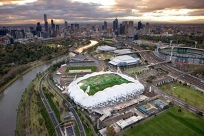 An aerial view of a stadium surrounded by a cityscape, with a river running alongside. - Cozy & Chic Apt Near Crown Casino & Southgate Mall (Southbank)