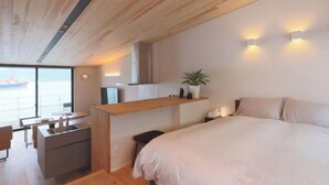 A modern hotel room with a wooden ceiling, a bed, a desk, a small kitchen area, and a large window with a view. - Dannoura Strait Villa (Shimonoseki)