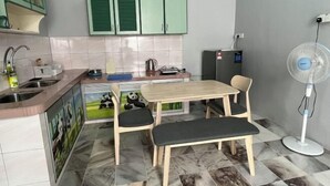 Una cocina compacta con gabinetes verdes, un lavamanos, un refrigerador, un ventilador y un comedor con mesa y sillas.