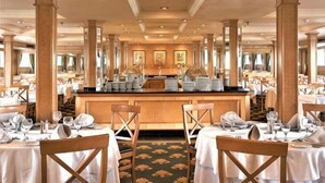 Une salle à manger élégante, avec des tables dressées pour le service, un bar central et une vue sur l’ensemble de la salle.