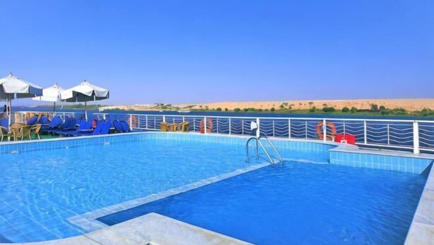 Une piscine aux carreaux bleus, un poste de surveillance pour les sauveteurs et des chaises longues.