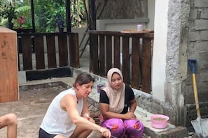 Two individuals seated on a concrete step outside a building with a wooden fence in the background. - Billi Family (Aik Berik)