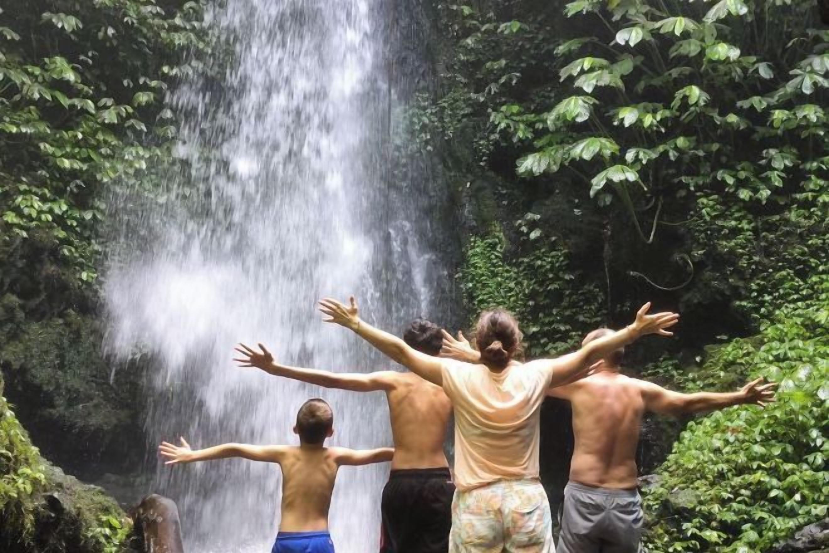 A group of people standing in front of a waterfall in a forested area.