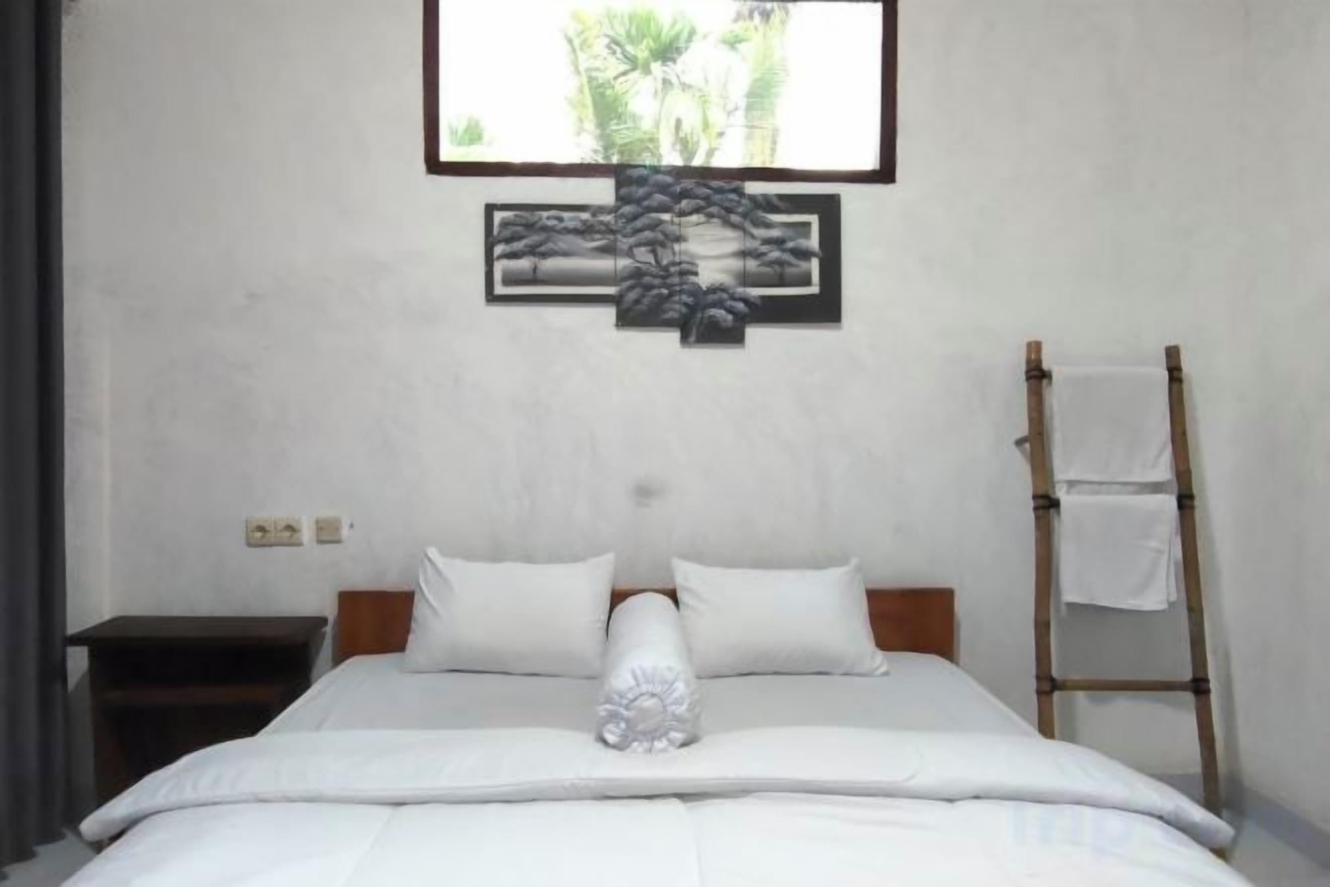 Una camera d'albergo con un letto, un comodino, una scala in legno e un'opera d'arte incorniciata appesa al muro.