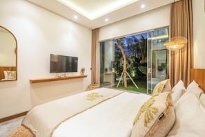 A bedroom with a large bed, a TV, a sliding glass door to a balcony, and a ceiling light fixture.
