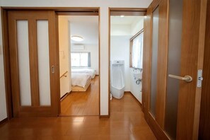 A hallway with wooden flooring leading to a bedroom with a bed and a bathroom with a bathtub and toilet. - lami home (Tokyo)