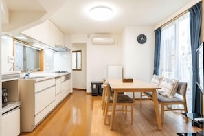 A compact kitchen with a sink, stove, and cabinets, a dining table with chairs, and a large window with curtains. - lami home (Tokyo)