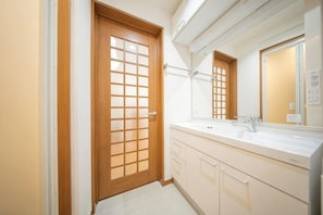 A bathroom with a wooden door, a sink, a mirror, and cabinets.