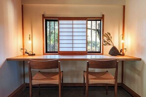 A room with a wooden desk, two chairs, a shoji screen, and a vase with dried plants. - KEYAKIZAKA (Ito)